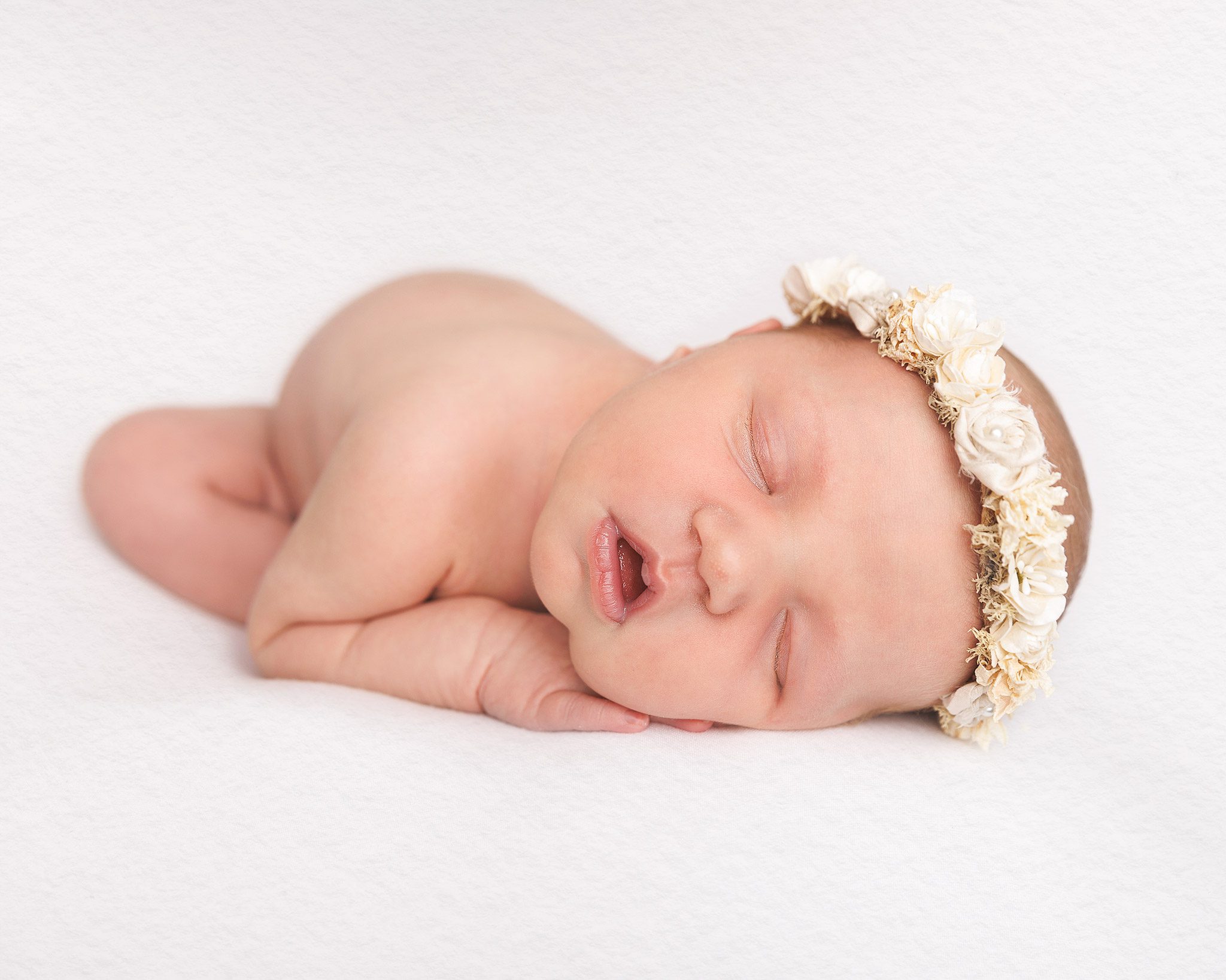 8 day old baby girl sleeping for her photograph with a beautiful headband on for added decoration