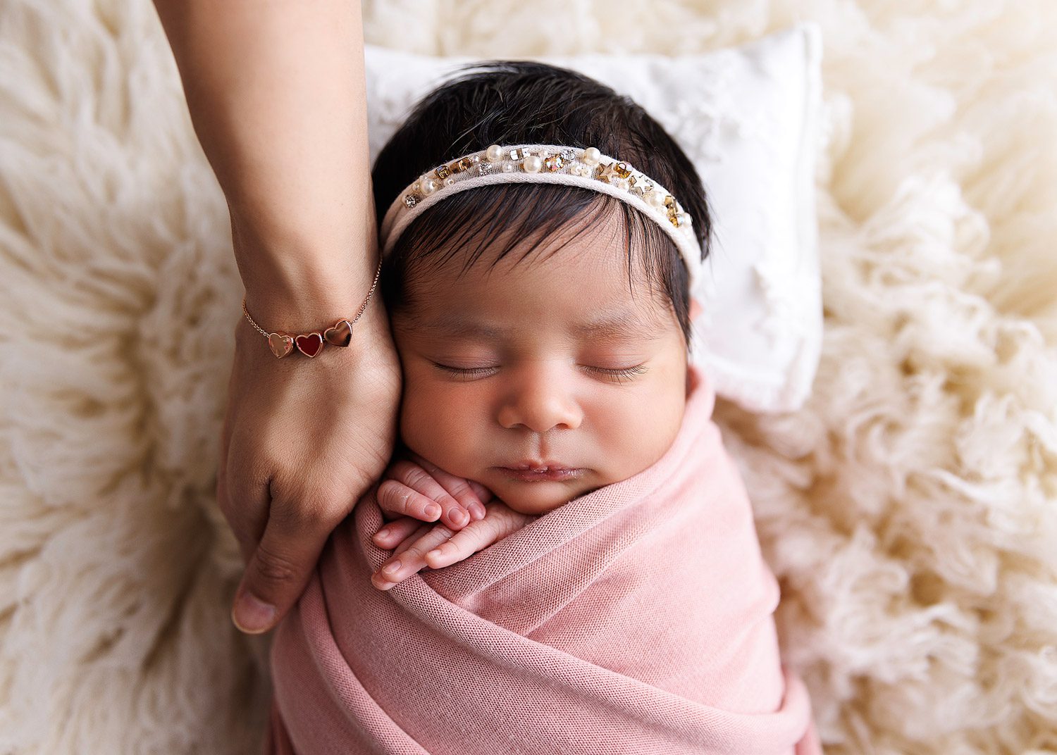 Newborn Baby girl wrapped in a pink swaddle with mums hand lovingly touching her face in a relaxing studio by Woking town centre